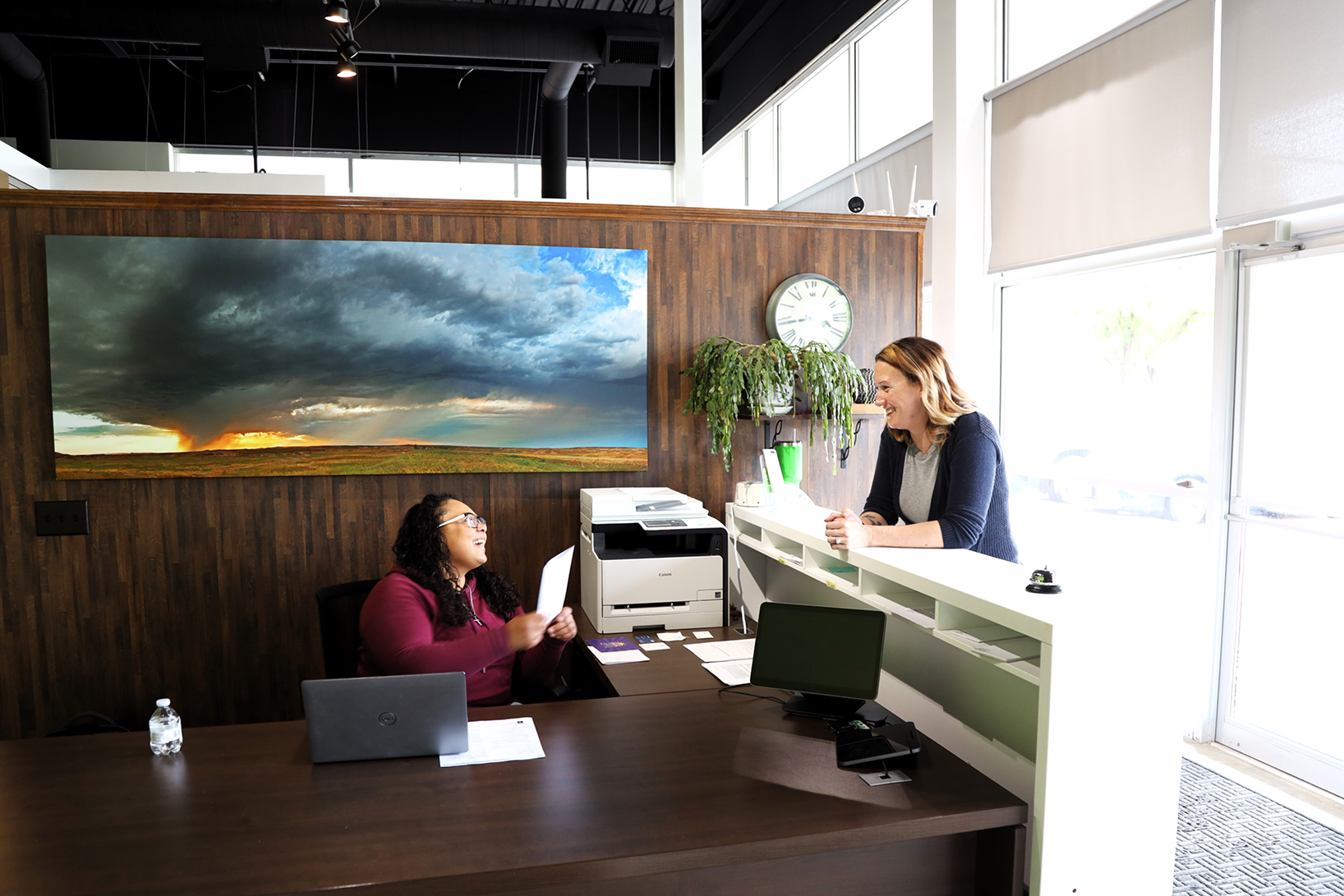 Photo of woman being greeted in bright, modern office by another woman sitting behind a desk