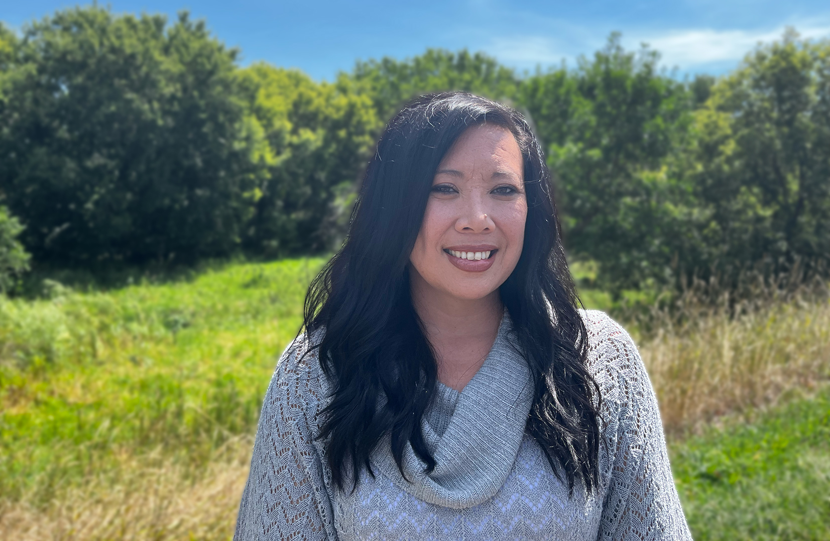 Photo of woman with dark hair outside in front of greenery
