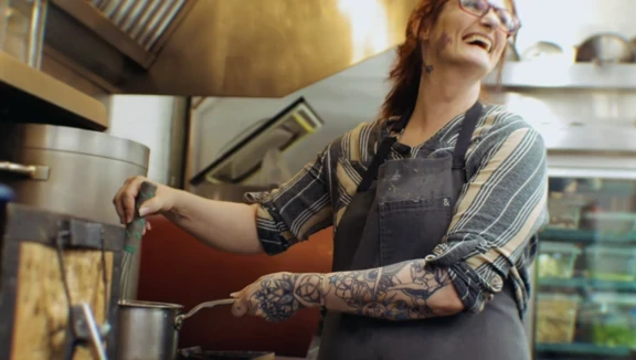 Photo of woman laughing while stirring something on the stove