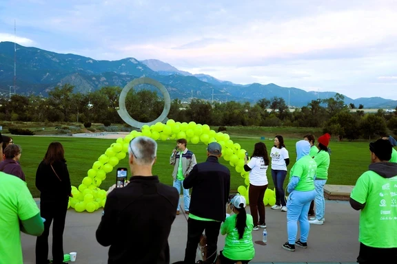 Photo of man speaking in front of green balloon arch