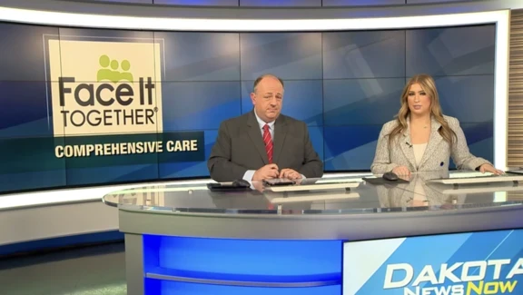 Photo of a man and women sitting at a broadcast desk